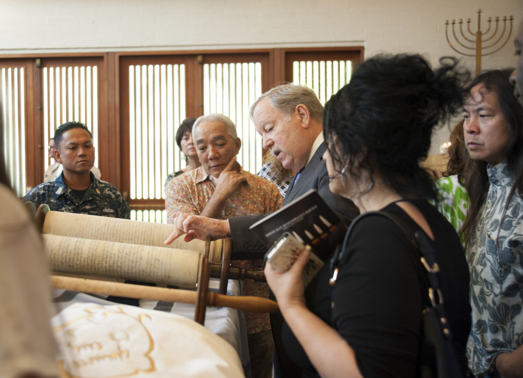 Room full of people looking at a copy of the torah