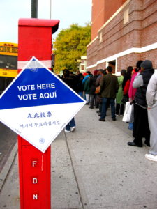 People waiting in line with a sign that reads "Vote Here, Vote Aqui"