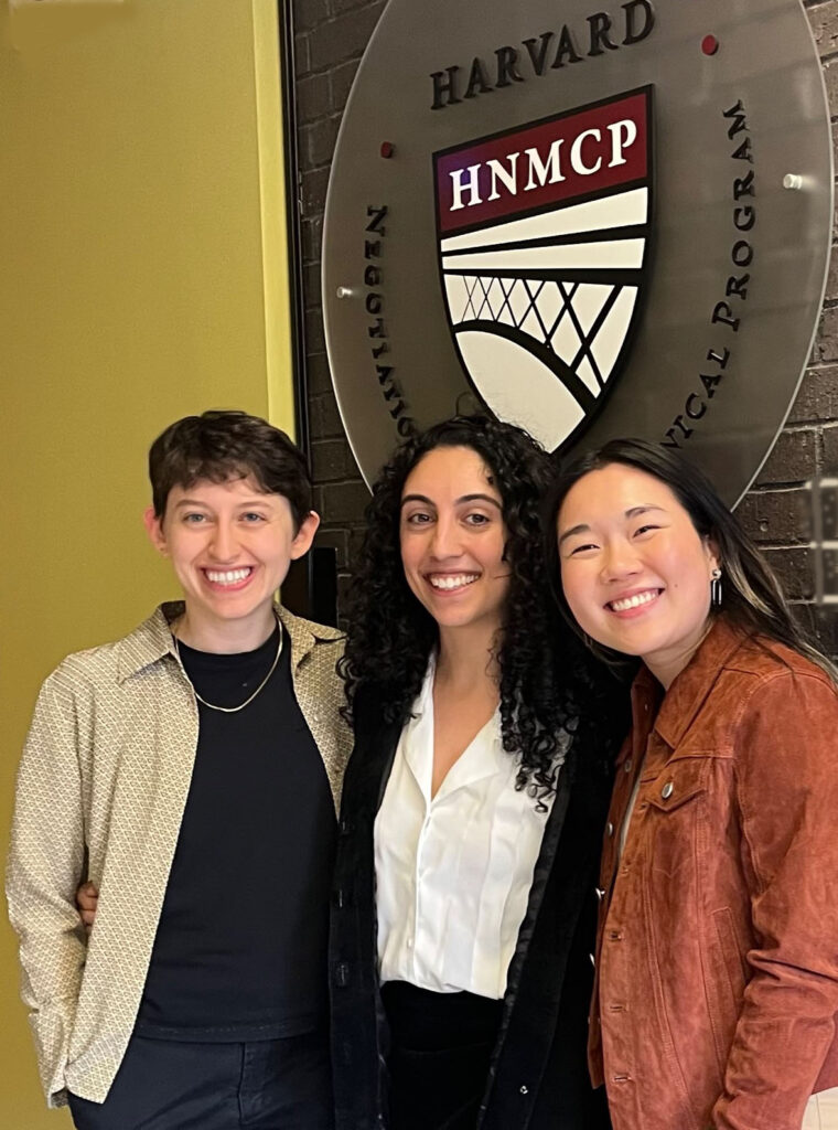 Three women standing in front of an HNMCP logo