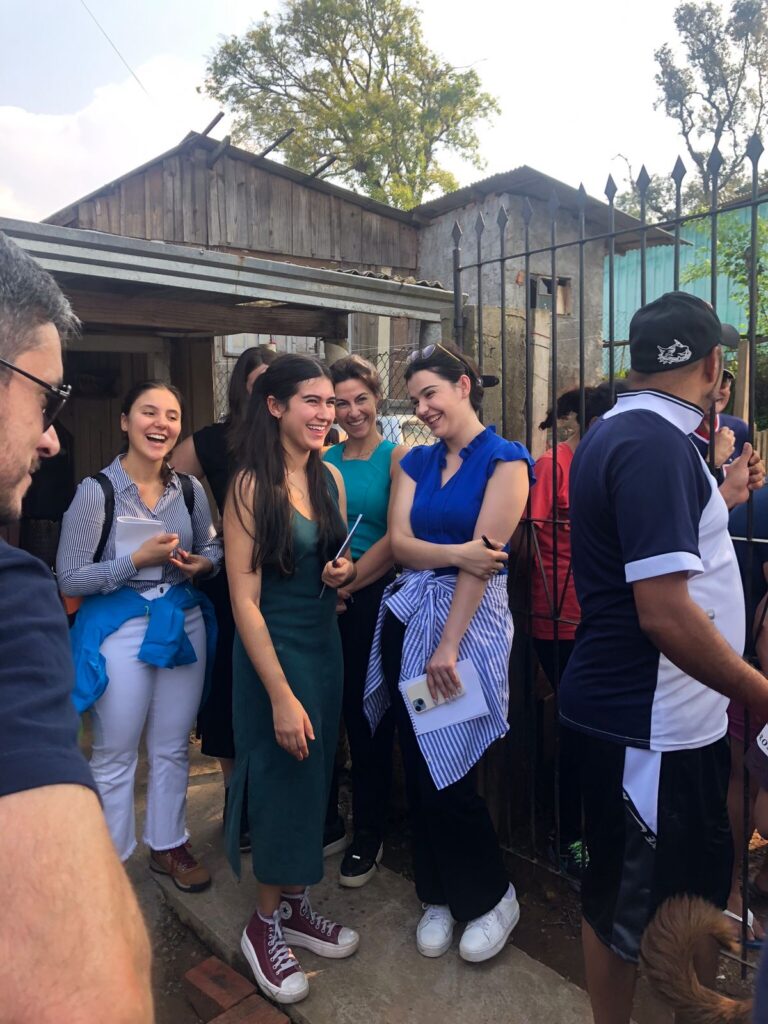 Two images. The first of the student team of three women standing together laughing. The second is the three students, the two faculty, and several local children all together smiling.