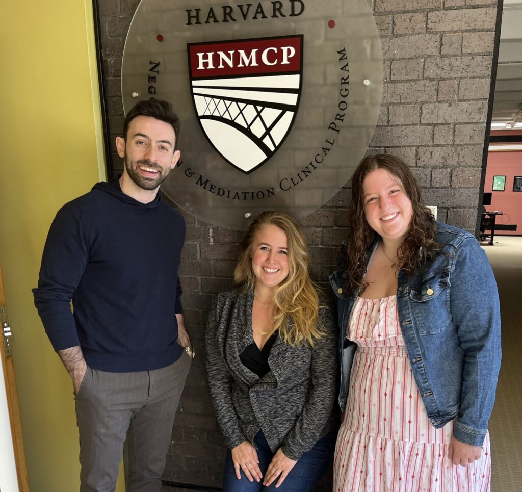 A man and two women standing in front of the HNMCP logo, smiling.
