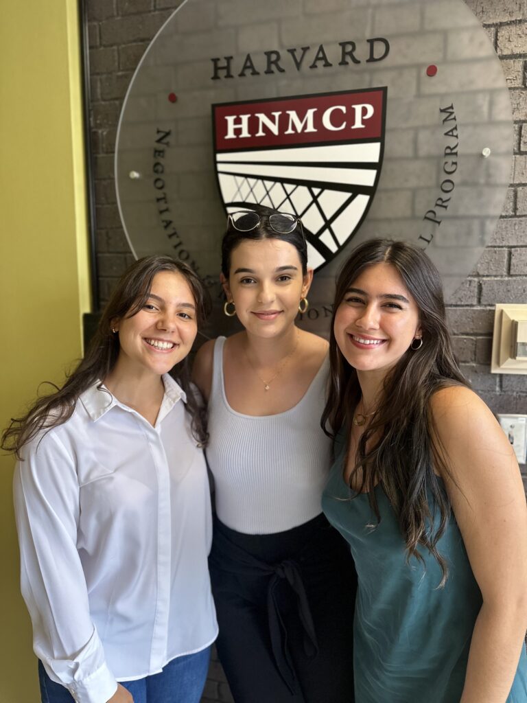 Three young women standing in front of the HNMCP logo