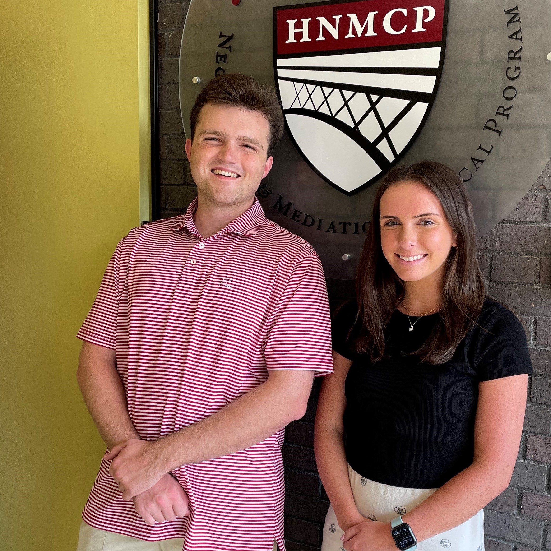 A man and a woman standing in front of the HNMCP logo