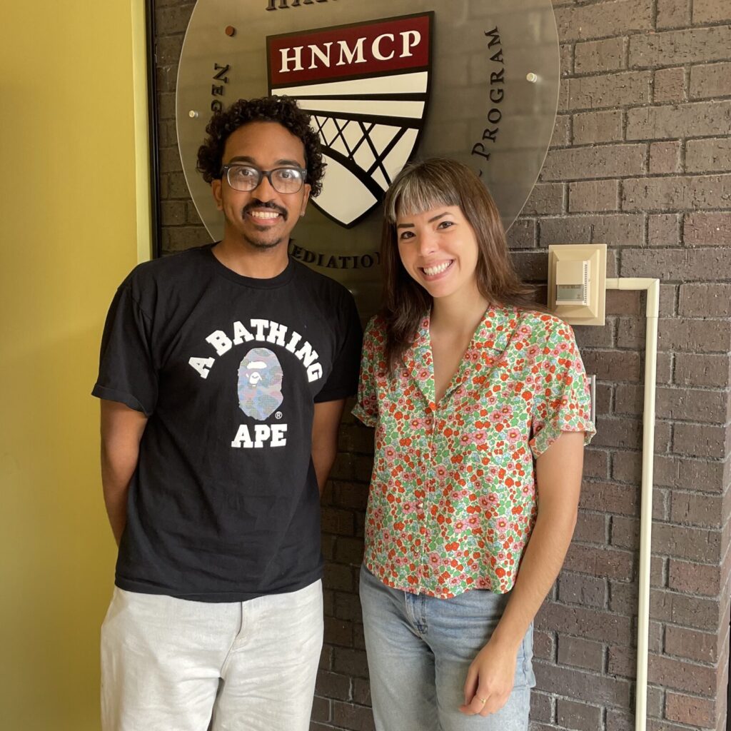 A man and a woman, smiling, stand in front of the HNMCP logo