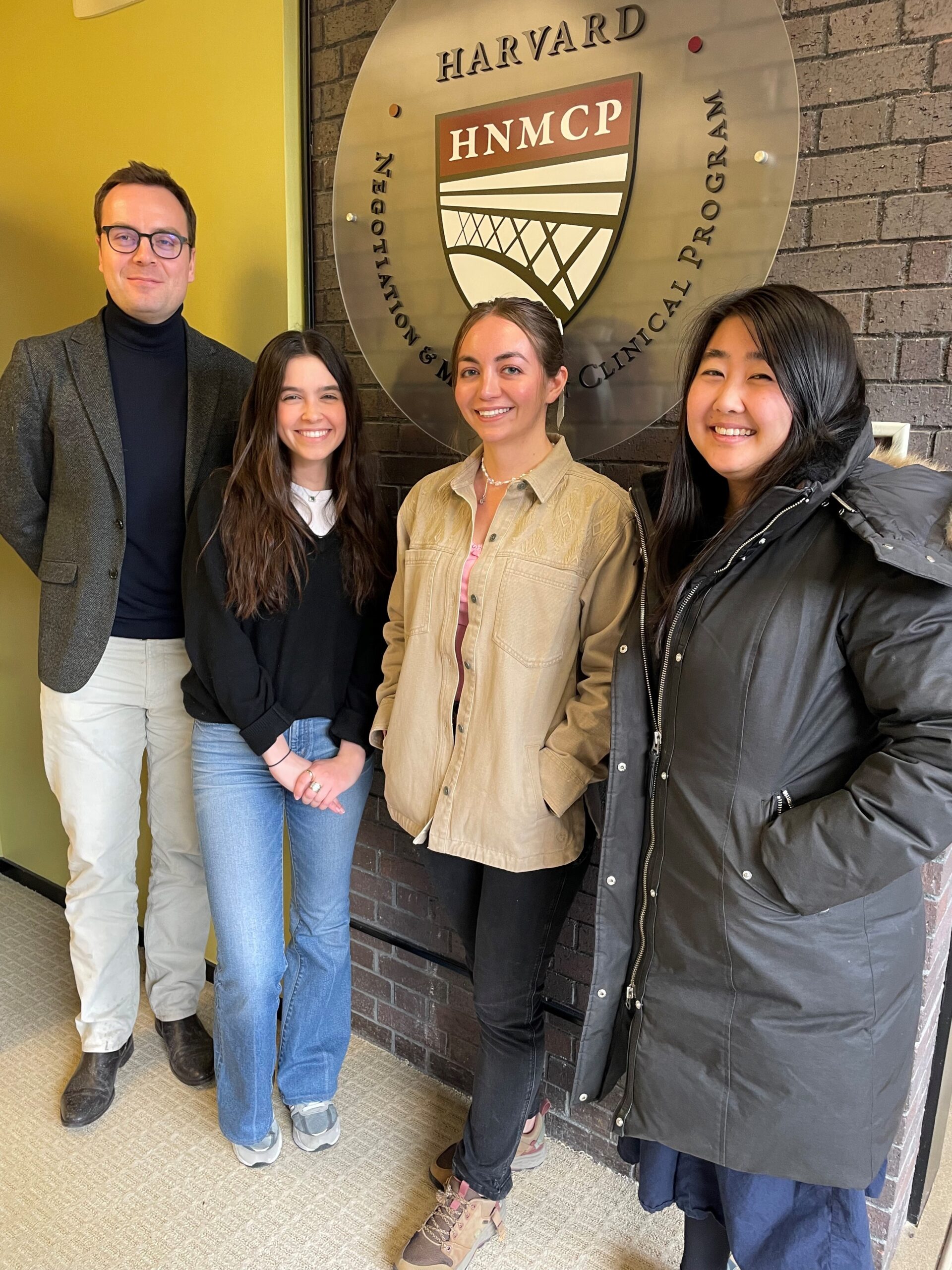 A tall man and three women standing in front of the HNMCP logo