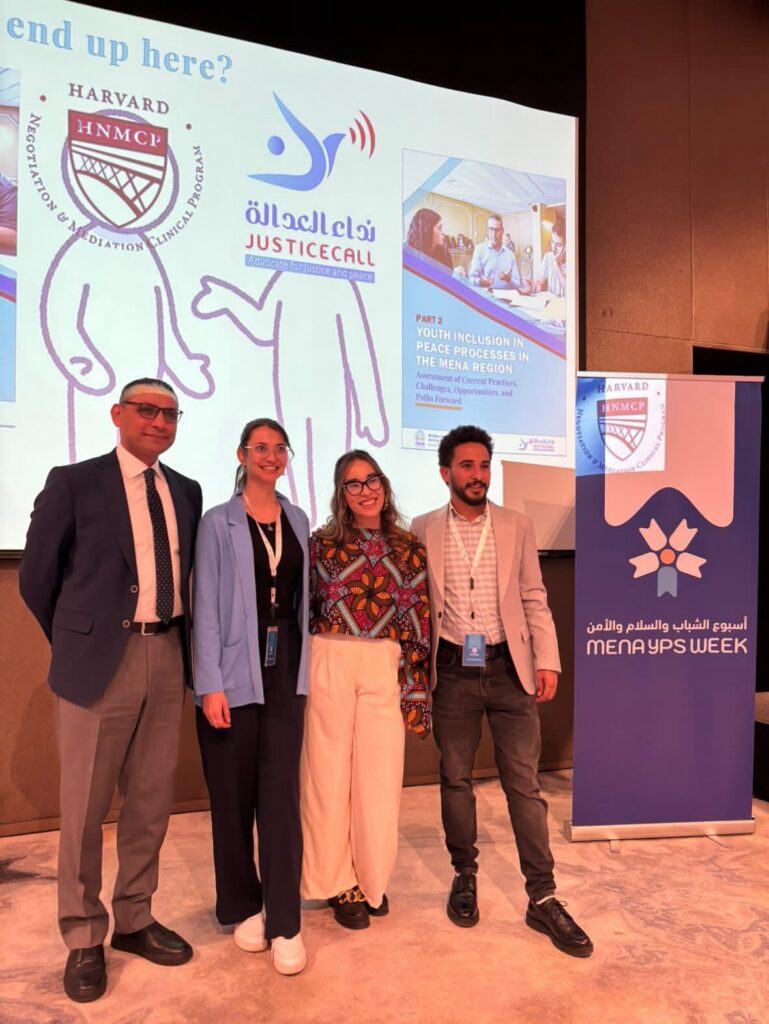 A man, two women, and another man standing on a stage with a slide show behind them.